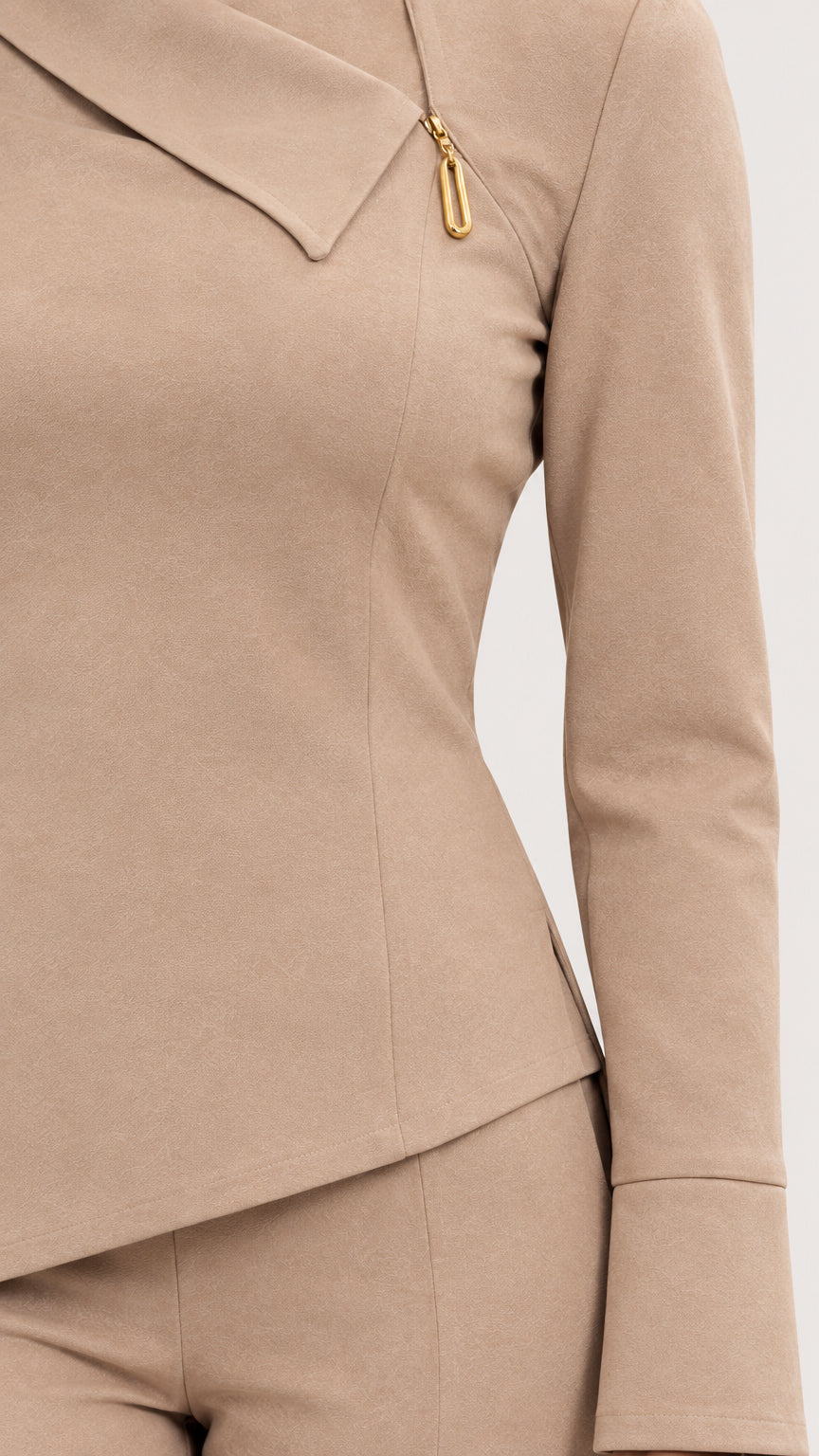 Close-up detail of beige asymmetrical folded neckline with gold-tone zipper pull accent